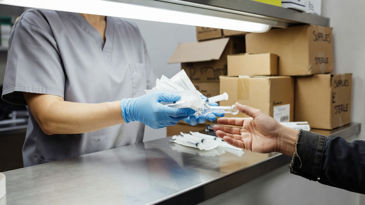 Photo illustration: a gloved worker hands a glass pipe and syringes across a sterile-supply counter